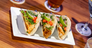 three tacos on a plate with beer and margarita specials